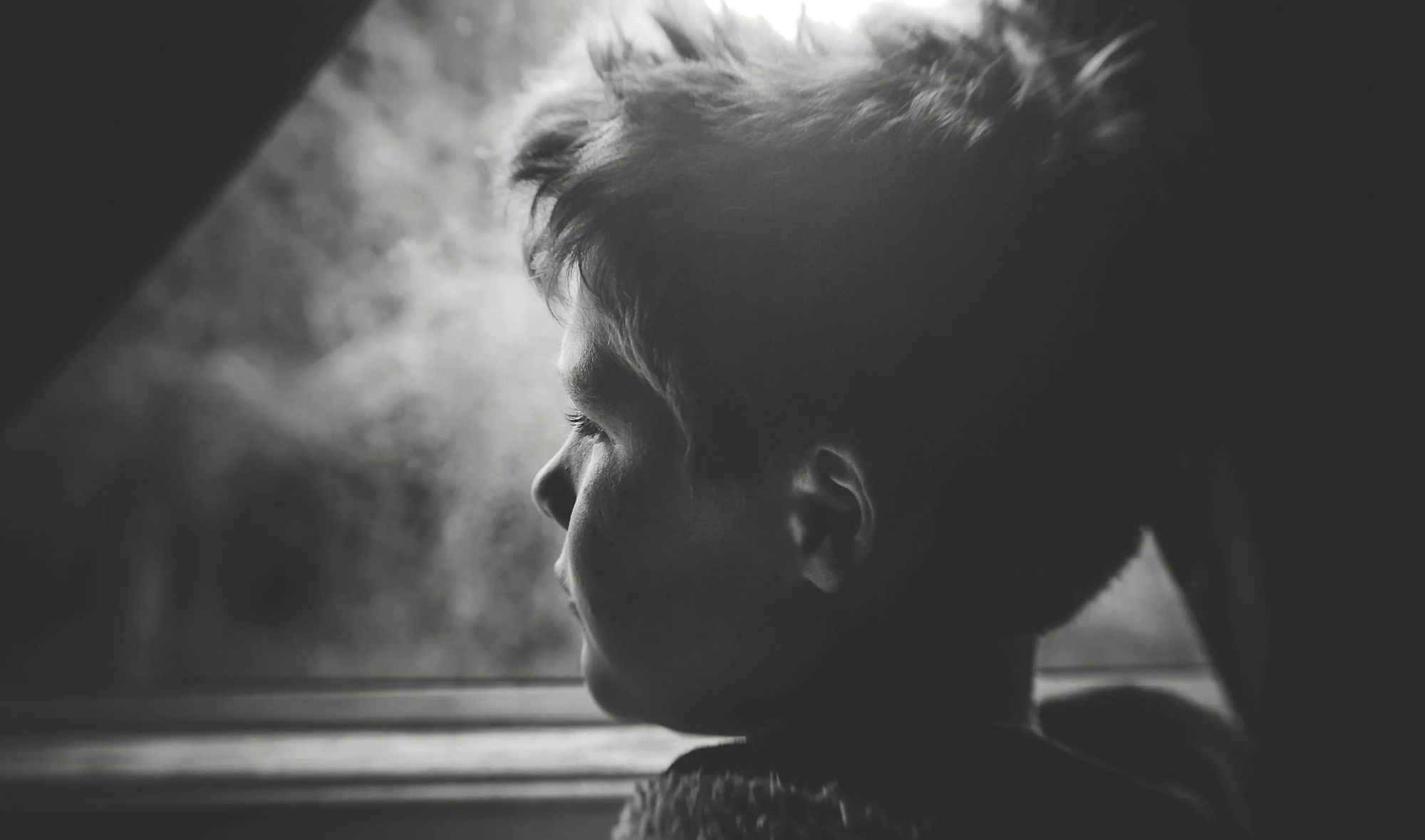 Boy looking out a window in a black-and-white photograph